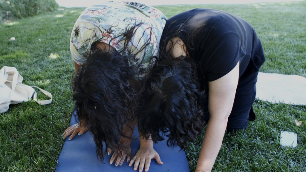 Photo of two people on all fours with their heads down. their shoulders and arms pressed close.